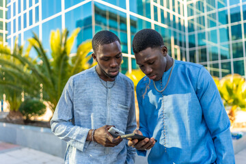 Senegalese businessmen wearing traditional dashiki using smartphones in front of office building © unai