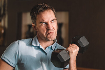 Handsome power man in training pumping up muscles with dumbbell. Home exercise. Sports lifestyle....