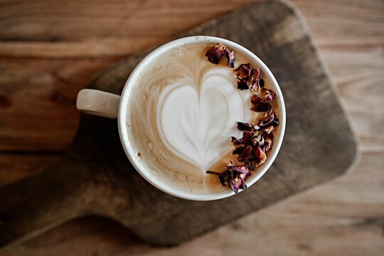 Top view of a cup of latte art coffee with dried rose petals on a wooden board