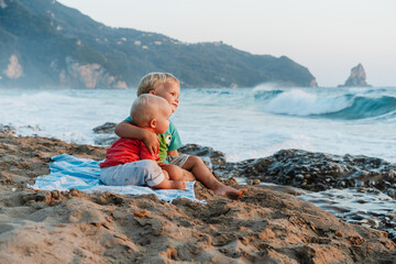 Two happy little children sitting on beach and looking at ocean.
