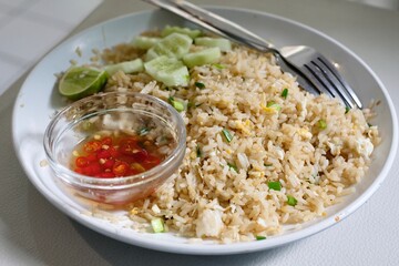 A plate of crab fried rice with fresh cucumber slices, lime, and chilli fish sauce at a street food stall in Silom - Bang Rak, Bangkok, Thailand
