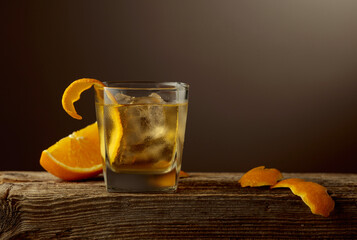 Old Fashioned cocktail with a ice, garnished with an orange peel on a old wooden board.