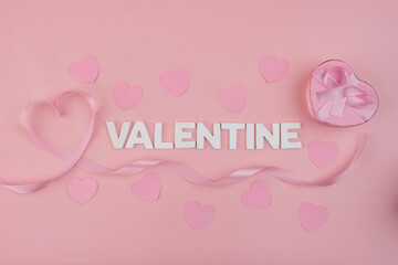 A pink ribbon forming a heart shape next to the word VALENTINE and a heart shaped gift box surrounded by small paper hearts
