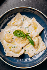 Creamy ravioli garnished with fresh basil leaves served on a blue plate, an Italian culinary delight