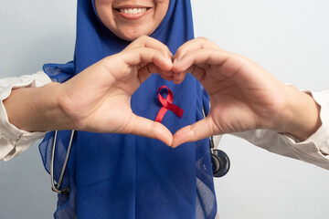 Happy Muslim Female Asian doctor or nurse hand in love or heart with Red ribbons, HIV awareness concept, world AIDS day, world cancer day.