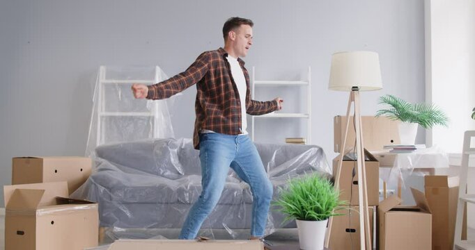 Happy new flat owner, apartment renter man moving, dancing carrying tripod floor lamp to furnish new living room in new house with modern comfort furniture, getting bank loan for interior design 