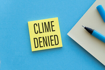 Paper notes with the words Clime Denied on Yellow Sticky on blue table, top view.