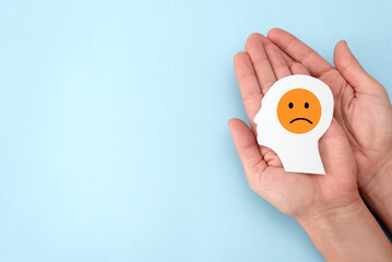 Close up of Hands holding paper human head with sad orange emoji on blue background