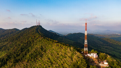 Obraz premium A panoramic aerial view of a telecommunications tower standing tall on a lush green mountaintop against a clear blue sky.