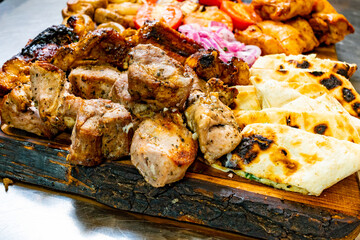 Grilled meat platter with flatbreads and vegetables served on wooden board