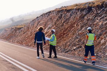 Fototapeta premium Three engineers, including a Muslim woman, walk together in the early morning, reviewing and analyzing wind turbine project plans while discussing innovative solutions on site.
