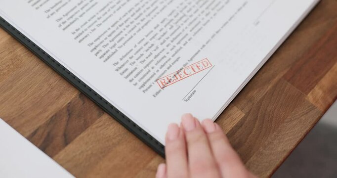 Woman hand puts stamp with word Rejected on contract. Female entrepreneur refuses to cooperate with partner due to unprofitable terms slow motion