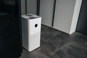 Stylish air purifier in the interior of a room with a gray floor and white walls. Technologies and health.