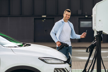 Happy man holding EV charger plug for electric vehicle using mobile phone for payment
