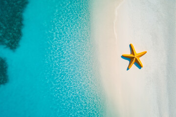 Aerial view of a yellow starfish lying on a beautiful white sand beach next to crystal clear turquoise water
