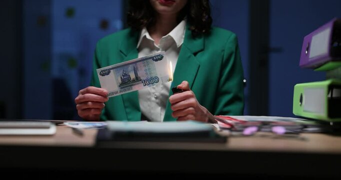 Woman burns Russian ruble banknote with lighter symbolizing financial crisis. Economic downturn and loss of monetary value concept slow motion