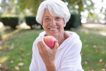 senior woman in the park enjoying an apple