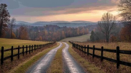 Fototapeta premium Winding gravel road through autumn fields leading to misty mountains at dawn