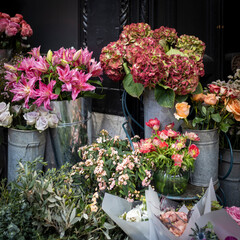 Elegant burgundy lilies arranged alongside hydrangeas, red anemones, buttercups, and orange roses, adorned with eucalyptus branches, ideal for interior decoration and special occasions like weddings, 