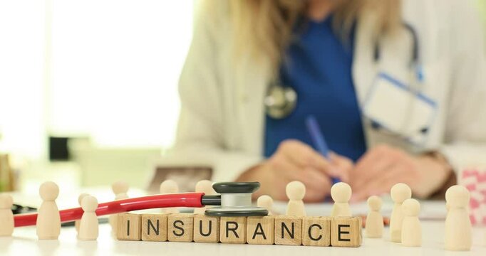 Text Insurance on wood block with pawns and stethoscope against working doctor. Financial coverage of healthcare service for patients concept