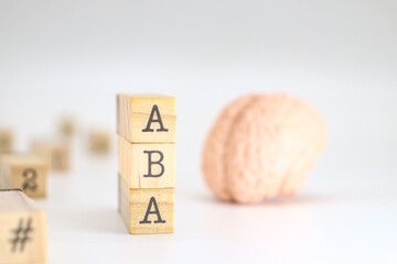 Applied behavior analysis acronym. ABA written on wooden cubes isolated with a figure of a brain on white background with space for text.