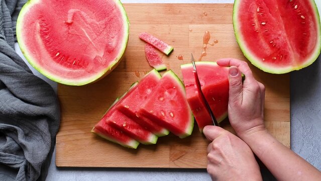 Female hands cutting fresh juicy watermelon slices on cutting board.