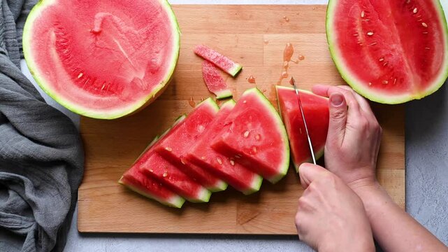 Female hands cutting fresh juicy watermelon slices on cutting board.