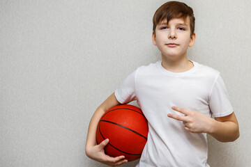 teenage boy in white t-shirt holds orange basketball under arm and shows two fingers
