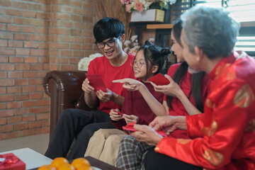 happy asian family gathering at home to celebrate Chinese New Year,sitting on couch,talking,giving red envelope and eating