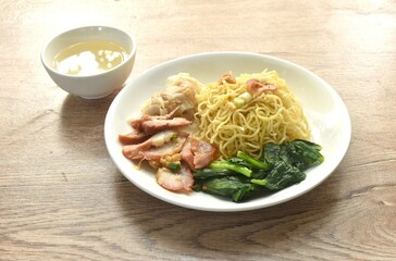 dry Chinese egg yellow noodles with red barbecue pork and dumpling in on plate with clear soup cup