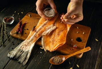 Hands skillfully season a fresh piece of smoked salmon with salt and spices in a rustic kitchen....