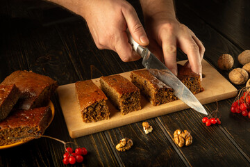 Hands skillfully cut thick slices of freshly baked cake on a wooden board adorned with walnuts and...