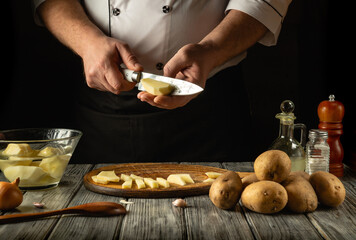 In a warmly lit kitchen, a skilled cook carefully slices fresh potatoes, preparing for a delicious meal. European cuisine