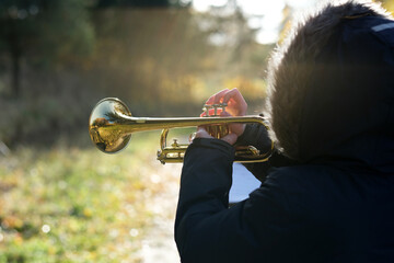 A boy playing trumpet while wearing a jacket on the background of the rays of the sun, turned...
