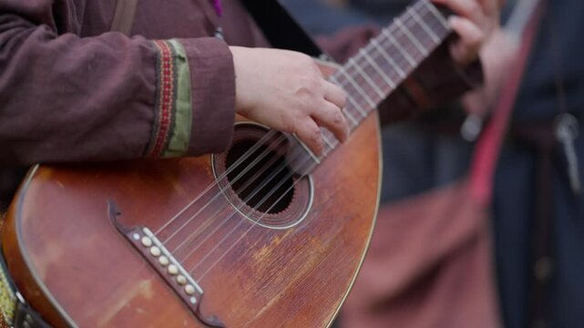 A man is playing a guitar with a strap around his neck. The guitar is an old one and the man is playing it with a lot of passion