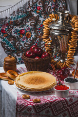 Pancakes on the table with traditional patterns, next to the samovar, apples and caviar