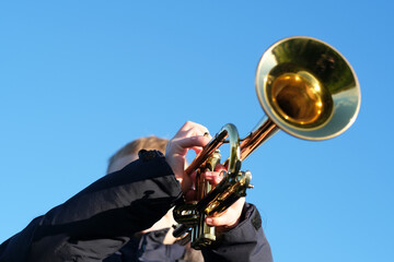 A boy playing trumpet on the background of the blue sky, bottom view. Calm autumn day, showcasing a love for music and nature. © HalynaRom