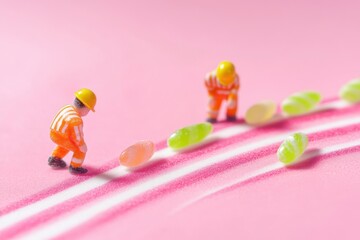 Fototapeta premium Miniature workers with candy beans on pink background
