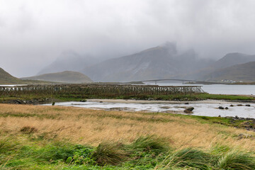 Panoramic view over the water and landscape with traditional racks for drying fish near Ramberg, Norway on the Lofoten island chain archipelago with Flakstad bridge in background