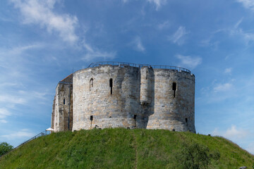 Low angle view of York Castle a ruined keep or fortification of medieval Norman castle or Clifford's Tower in the city of York, England against a white clouded blue sky