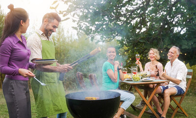 Family and friends gathering together grilling food and drinking wine in the garden during a barbecue celebration party
