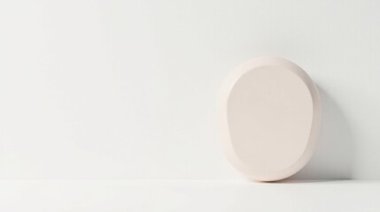 A pale pink oval object rests on a white surface against a minimalist backdrop