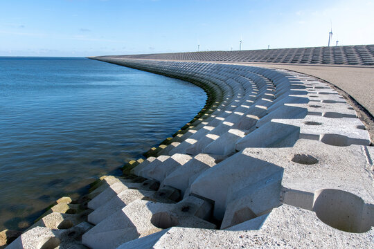 Curved dike body with concrete blocks near port of escape on former Breezand working island on Afsluitdijk (dam separates IJsselmeer lake from Wadden Sea), the Netherlands against a clear blue sky