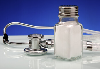 Glass salt shaker accompanied by a stethoscope symbolizing health awareness and sodium intake issues.