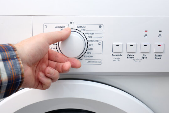 A man's hand sets the automatic washing program switch on the washing machine panel. Saving water and natural resources.