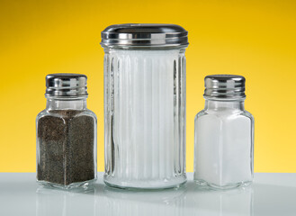Salt, pepper, and sugar shakers on a vibrant yellow background highlighting essential table condiments