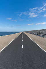 Low angle view of cycling path on Afsluitdijk (dam separates IJsselmeer lake from Wadden Sea), the Netherlands with dike body with concrete blocks against a clear blue sky