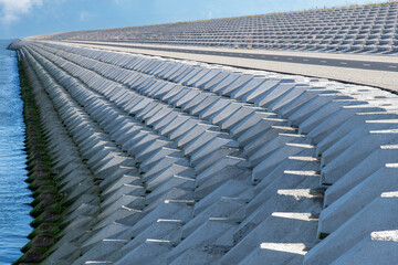 Fototapeta premium Curved dike body with concrete blocks near port of escape on former Breezand working island on Afsluitdijk (dam separates IJsselmeer lake from Wadden Sea), the Netherlands against a clear blue sky