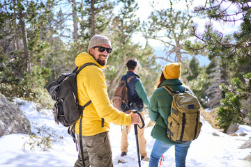 Caucasian man looking smiling at camera. At background, group of people hiking on snow mountain on holiday. Multiracial friends enjoying forest trail landscape