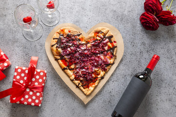 Food for Valentine's Day. Heart shaped sweet pizza with pineapple on gray background. View from above. Romantic dinner with red wine and gift.